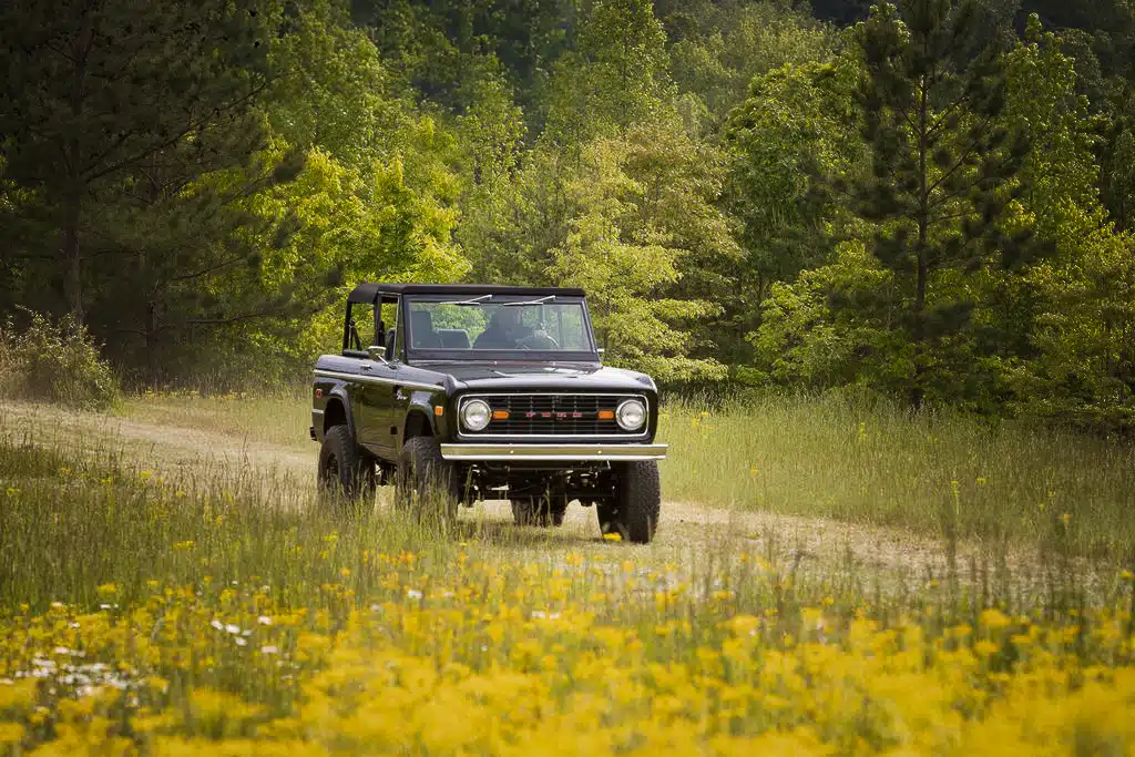 A first generation Ford Bronco driving on a dirt road
